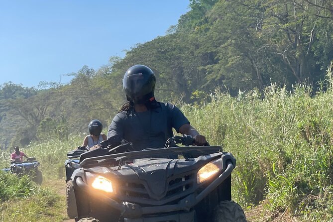 A helmeted rider on an ATV heading up a green hillside trail