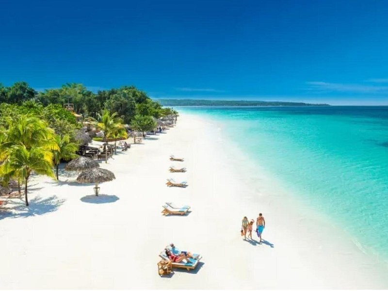 A white-sand beach curving away under palms beside clear Caribbean water
