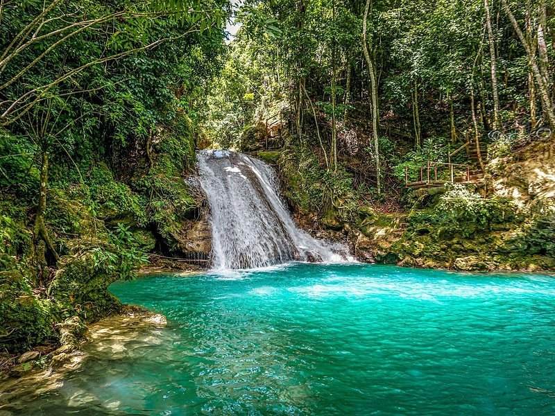 A jungle waterfall dropping into a bright blue-green swimming hole