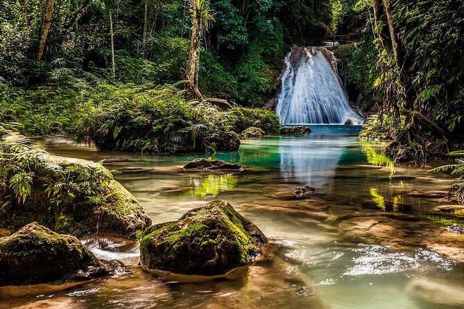 A jungle river with a waterfall and moss-covered boulders